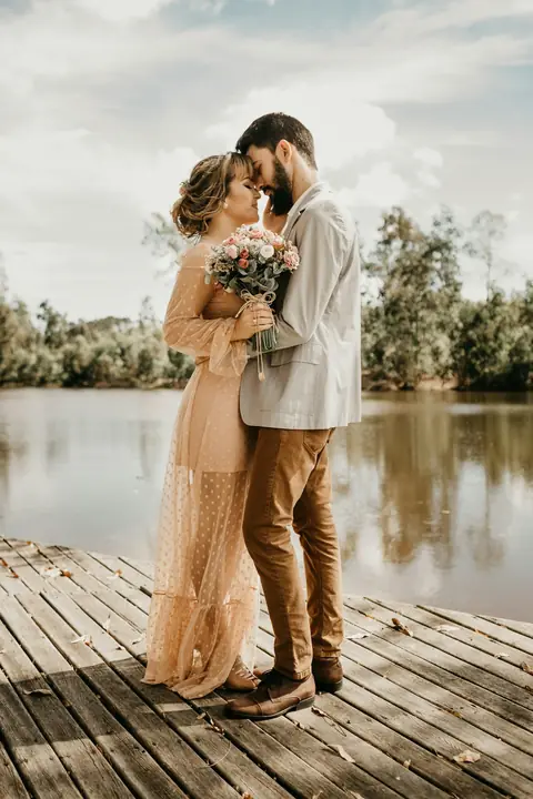 Pareja de novios abrazada sobre un muelle de madera junto al agua
