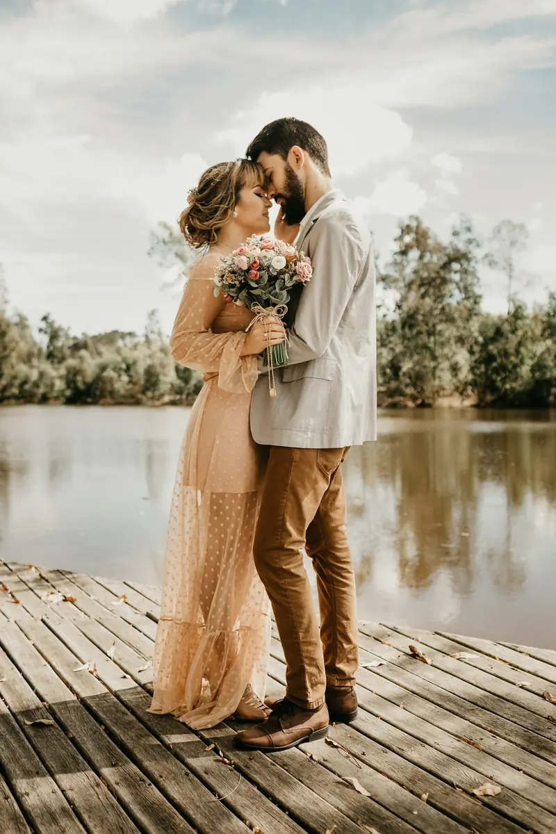 Pareja de novios abrazada sobre un muelle de madera junto al agua