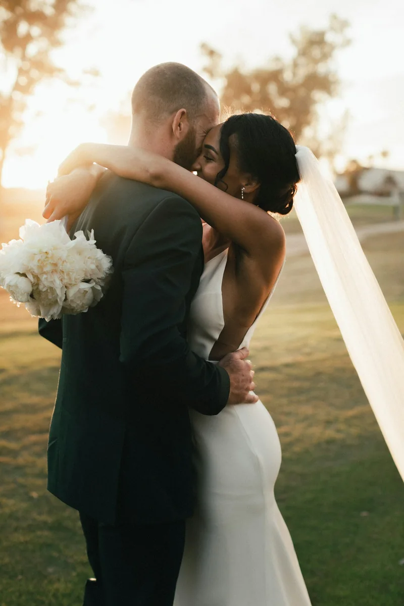 Novios abrazados al atardecer, ella con un ramo blanco