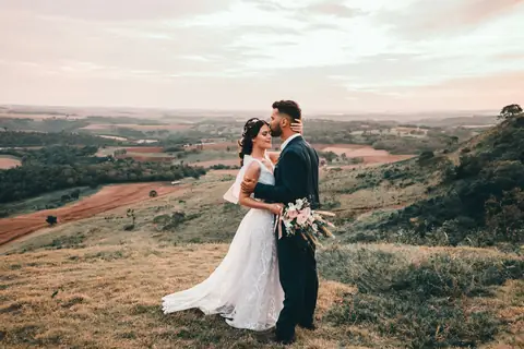 Novios en lo alto de una colina con el campo de fondo