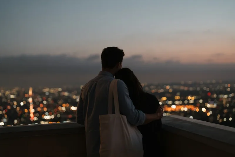 Pareja abrazada mirando las luces de la ciudad al anochecer