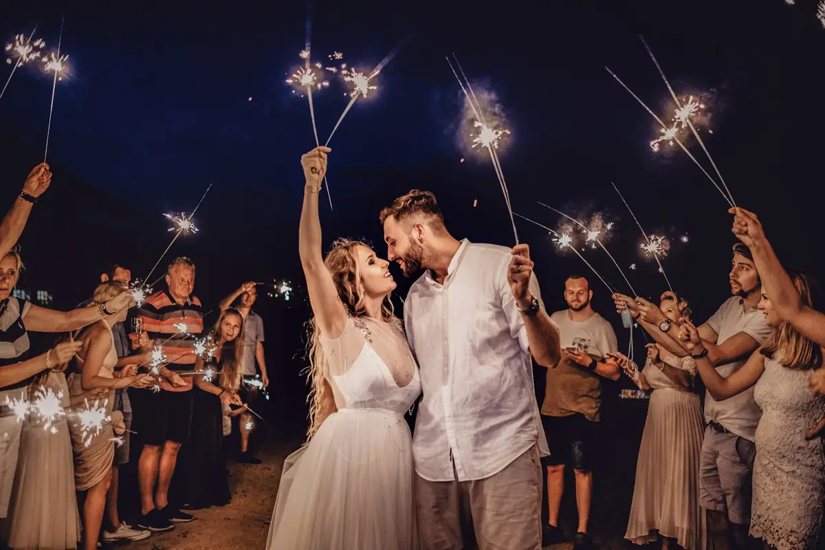 Novios entre invitados con bengalas encendidas, de noche