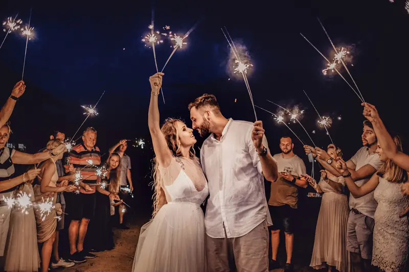 Novios entre invitados con bengalas encendidas, de noche