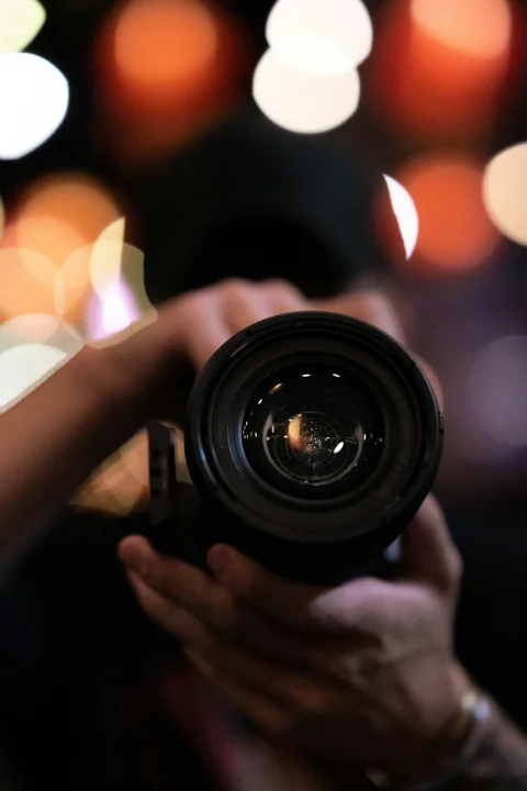 Persona apuntando una cámara hacia adelante, con luces de fondo